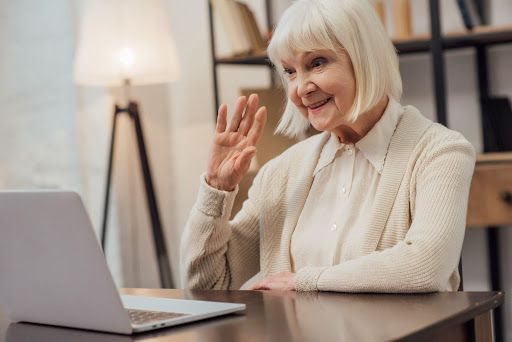 An older woman waving to her laptop camera.